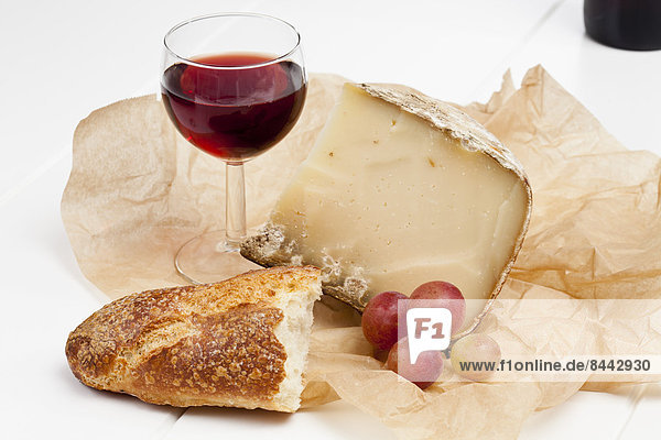 Französischer Schafskäse  fettdichtes Papier  Rotweinglas  Baguette und Trauben