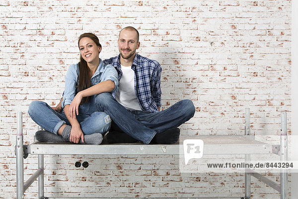 Junges Paar  das in ein neues Zuhause einzieht  auf einem Gestell sitzend