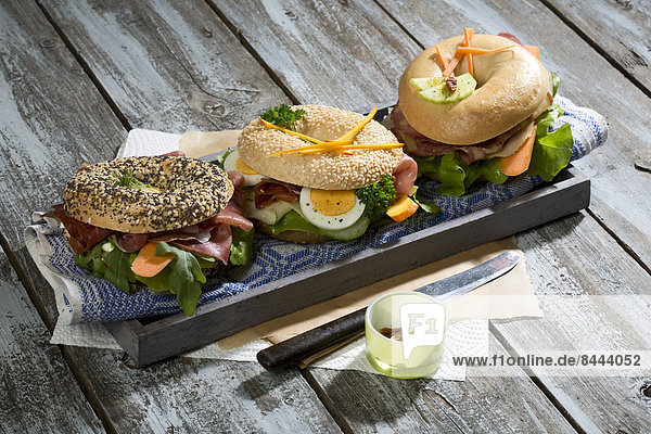 Three different bagels garnished with salami  sausage  slices of bacon  rocket salad  lettuce  cucumber carrot  egg  cream cheese and cress and parsley
