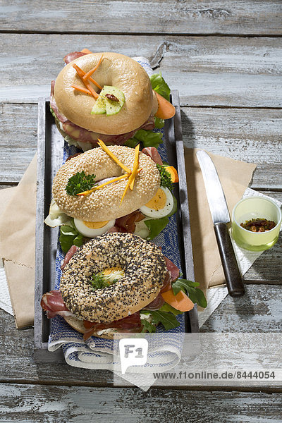 Drei verschiedene Bagels  garniert mit Salami  Wurst  Speckscheiben  Rucola  Salat  Gurkenkarotte  Ei  Frischkäse und Kresse und Petersilie.