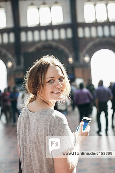 Porträt einer glücklichen Frau mit Handy am Bahnhof