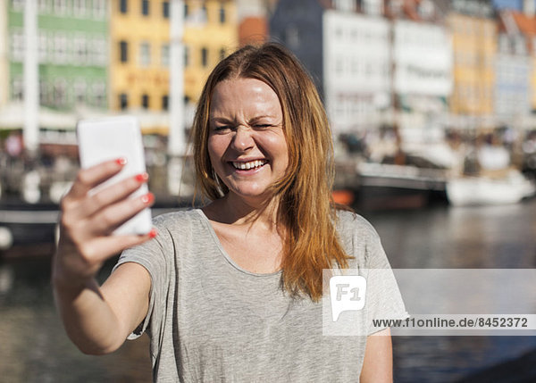 Happy woman photographing through smart phone at harbor