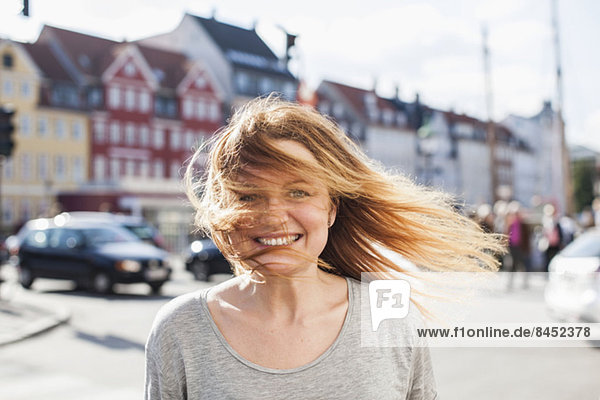 Porträt einer glücklichen Frau mit windgepeitschten Haaren auf der Stadtstraße