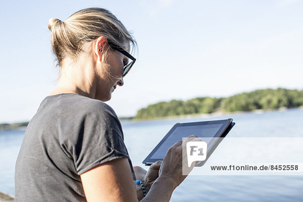 Mittlere erwachsene Frau mit digitalem Tablett am See
