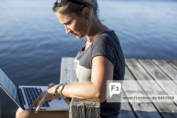 Side view of mid adult woman using laptop on pier
