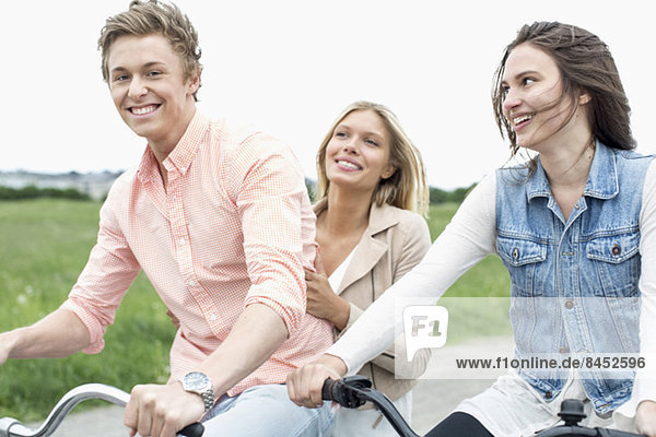 Porträt eines glücklichen Mannes  der mit Freundinnen auf dem Land Fahrrad fährt.