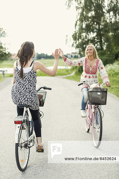 Glückliche Freundinnen geben High Five beim Radfahren auf der Landstraße