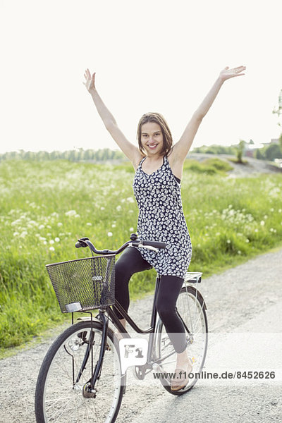 Porträt einer glücklichen Frau mit erhobenen Armen beim Radfahren auf der Landstraße