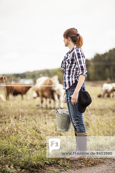 Bäuerin mit Eimer auf dem Feld stehend mit grasenden Tieren im Hintergrund