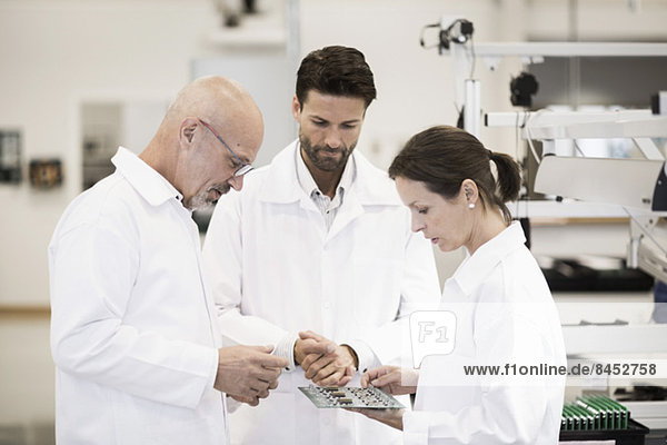 Team of technicians examining circuit board in factory