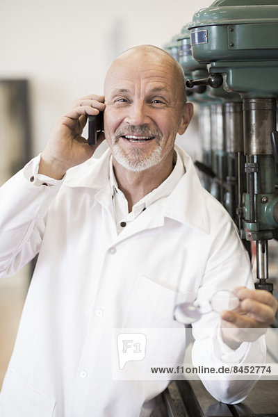 Porträt eines lächelnden Ingenieurs  der in der Fabrik auf das Handy geht.