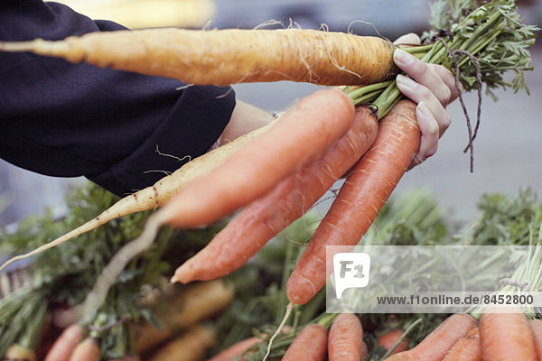 Abgeschnittenes Bild einer Frau  die Karotten am Gemüsestand kauft.