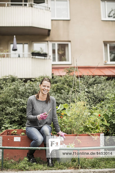 Ganzflächiges Porträt einer glücklichen Frau mit Gartengeräten im Garten