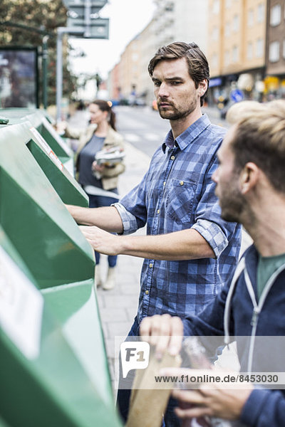 Young man with friends putting recyclable materials into recycling bins