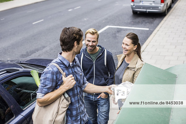 Happy friends with man putting newspaper in recycling bin