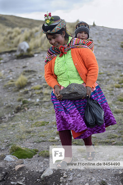 Young woman with child in a sling carrying a heavy stone to secure the shores of an artificial lake for irrigation  Quispillacta  Ayacucho  Peru