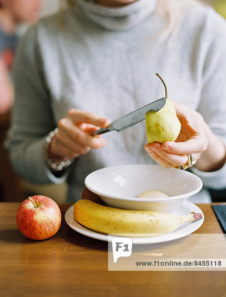 Eine Frau schneidet eine frische Birne in Scheiben. Apfel und Banane.