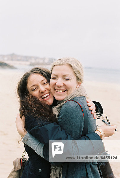 Zwei Frauen  die sich am Strand Wange an Wange umarmen.