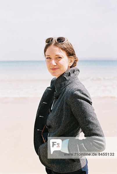 Eine Frau in einem grauen Mantel am Strand.