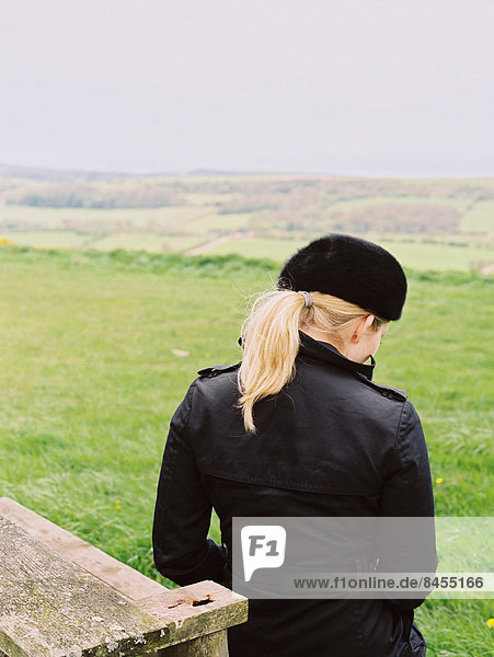 Eine Frau sitzt auf einer Bank und blickt über die Landschaft auf das Meer.
