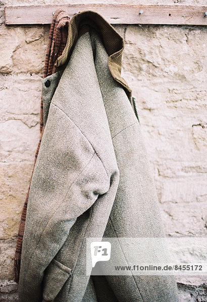 Eine traditionelle warme Jacke mit Cordkragen  die an einem Stift an einer Steinmauer hängt.