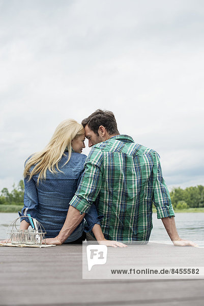 Ein Mann und eine Frau sitzen auf einem Steg an einem See.