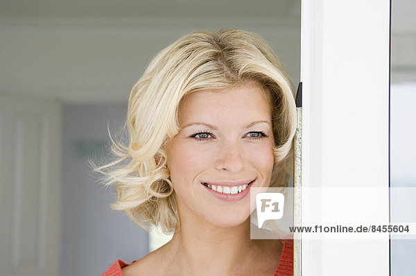 Eine junge Frau mit blonden Haaren lächelt in einer Türöffnung.