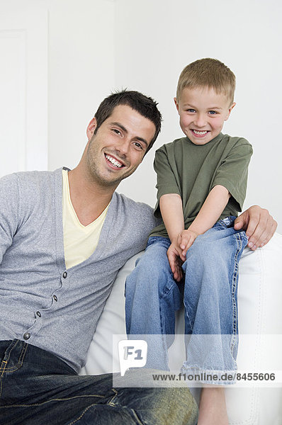 A man on a sofa beside a young boy wearing jeans.