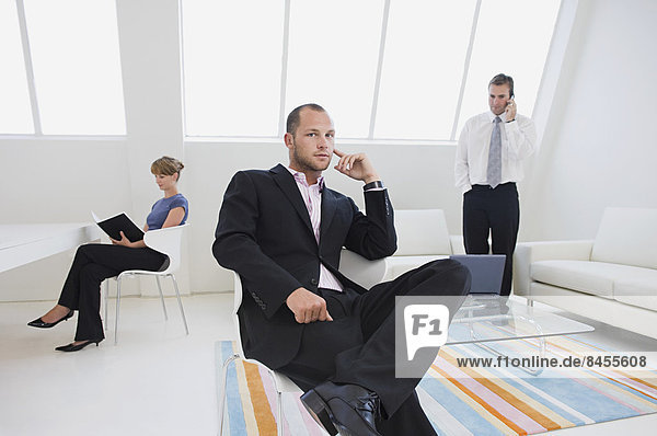 Three business people in an office  one on the phone  one working on a digital table  and one seated in a chair.