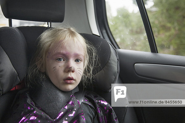 Ein junges Mädchen auf einem Autositz in einem Halloween-Kostüm.