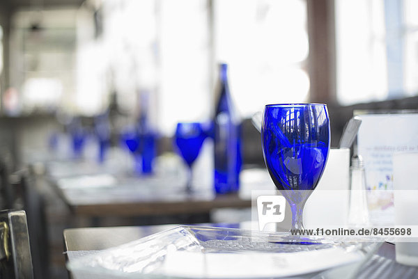A cafe interior. Bright blue glassware on empty tables.