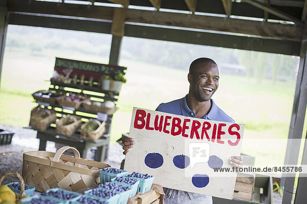 An organic fruit and vegetable farm. A person carrying a blueberries sign.