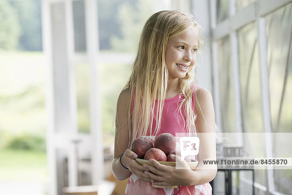 A young girl holding an armful of fresh peaches.