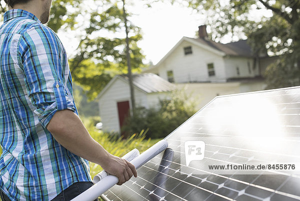 Ein Mann  der einen Plan zur Anbringung eines Solarpanels im Garten eines Bauernhauses verwendet.