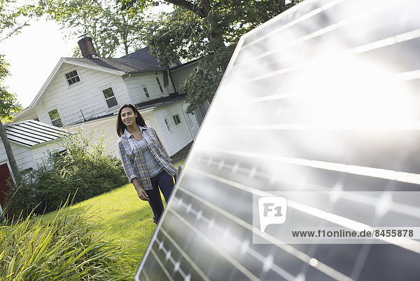 Eine Frau geht auf eine Solaranlage in einem Garten eines Bauernhauses zu.