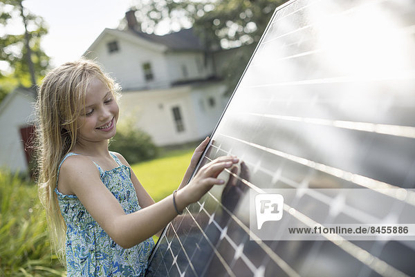 Ein junges Mädchen neben einem großen Sonnenkollektor in einem Bauerngarten.