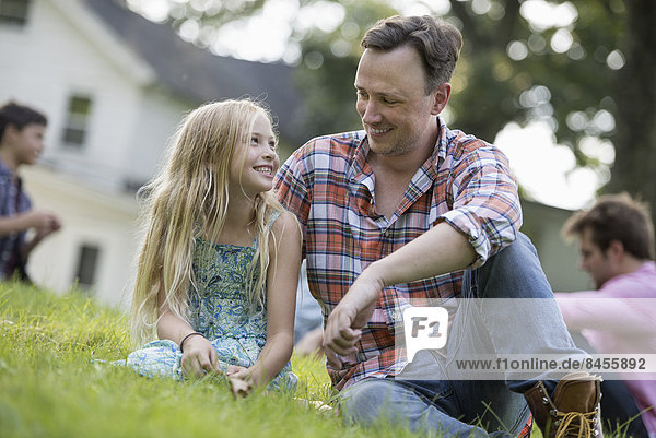 Ein Vater und eine Tochter auf einem Sommerfest  auf dem Rasen sitzend.