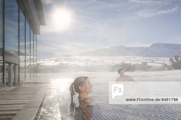 Woman and man sitting in a heated swimming pool in winter with steaming water  South Tyrol  Trentino-Alto Adige  Italy