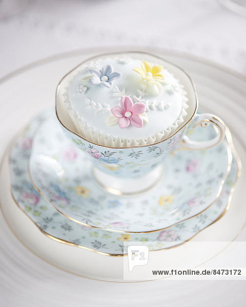 A floral china cup saucer and plates with iced cupcake