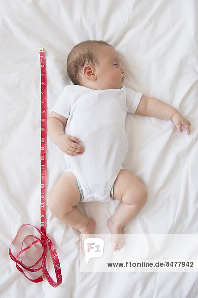 Baby girl (2-5 months) sleeping in bed with tape measure