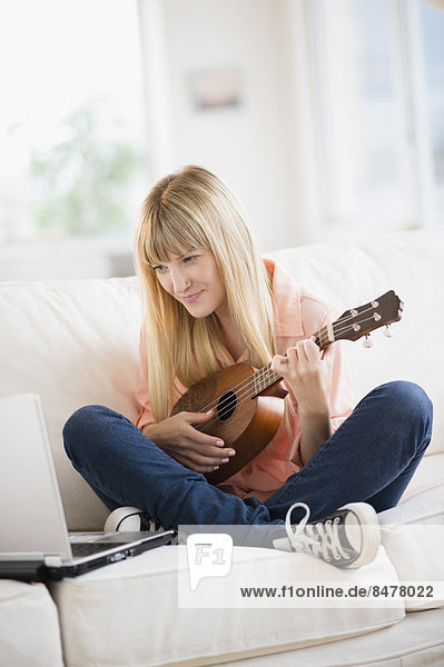 Woman playing ukulele while using laptop