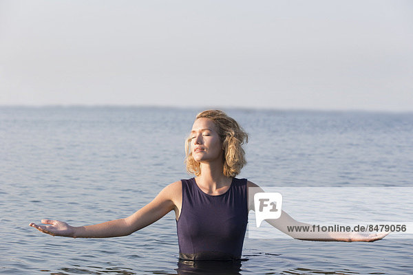Beautiful woman standing in lake with arms outstretched