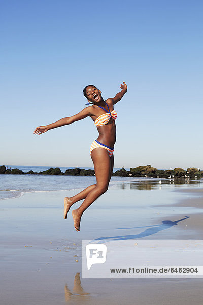 Black woman jumping for joy on beach
