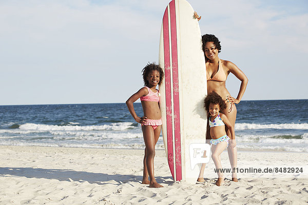 Mother and daughters with surfboard on beach