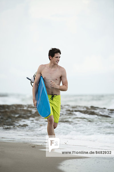 Hispanic man carrying surfboard on beach