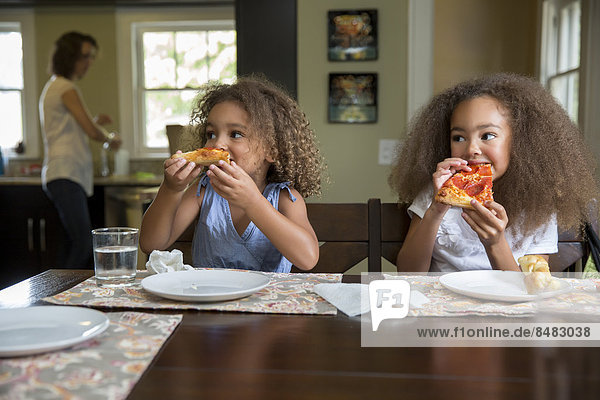 Mixed race girls eating pizza at table