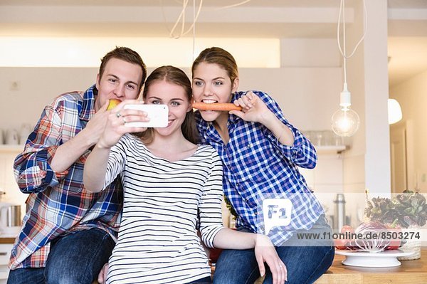 Three young people having fun taking photographs in the kitchen
