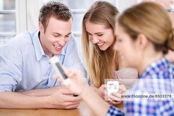Drei junge Leute schauen auf Handys und lächeln