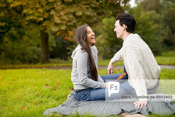 Young couple on blanket in park  laughing