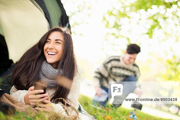 Young woman in tent using smartphone  laughing
